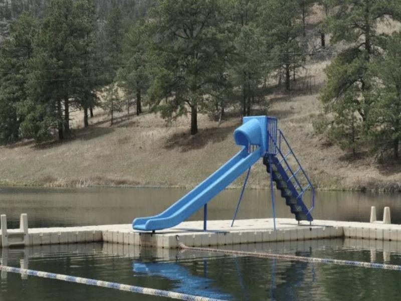 The swim dock and blue water slide on the lake below the pines
