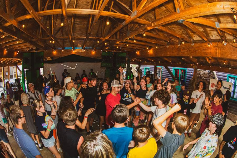 A packed pavilion of campers dancing under string lights
