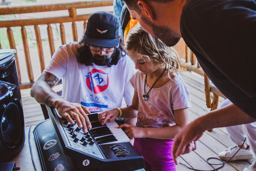 A mentor teaches a young camper chords on a keyboard