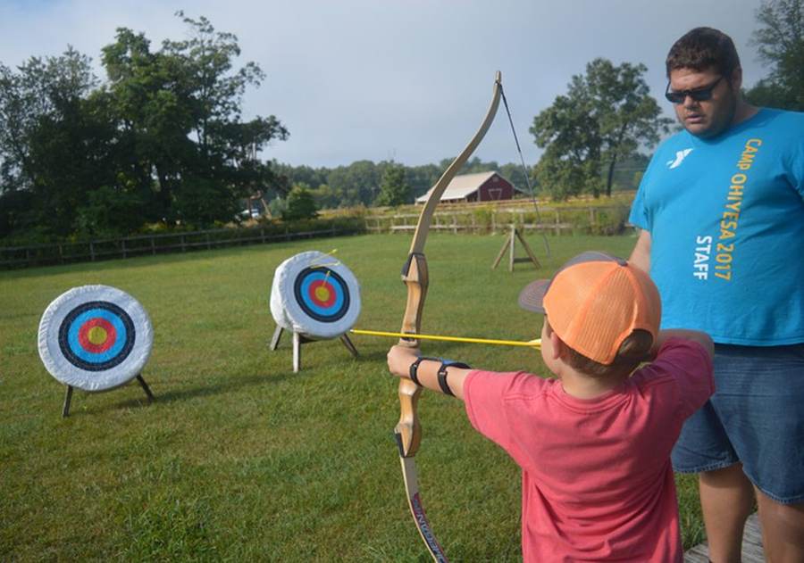 A counselor coaching a young camper at the archery range