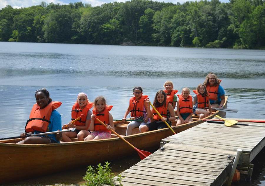A canoe full of campers in life jackets pushing off from the dock