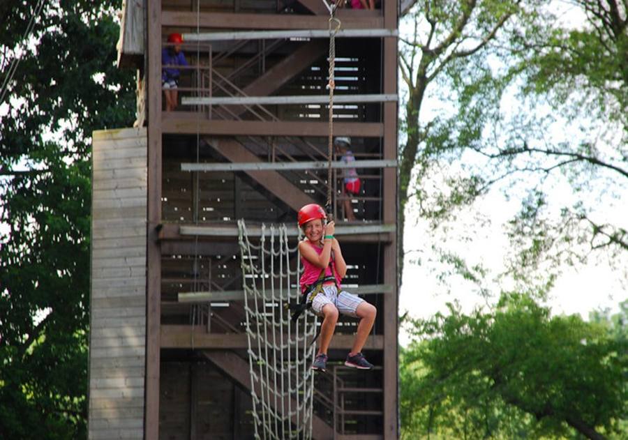 A camper climbing the cargo net on the tall climbing tower
