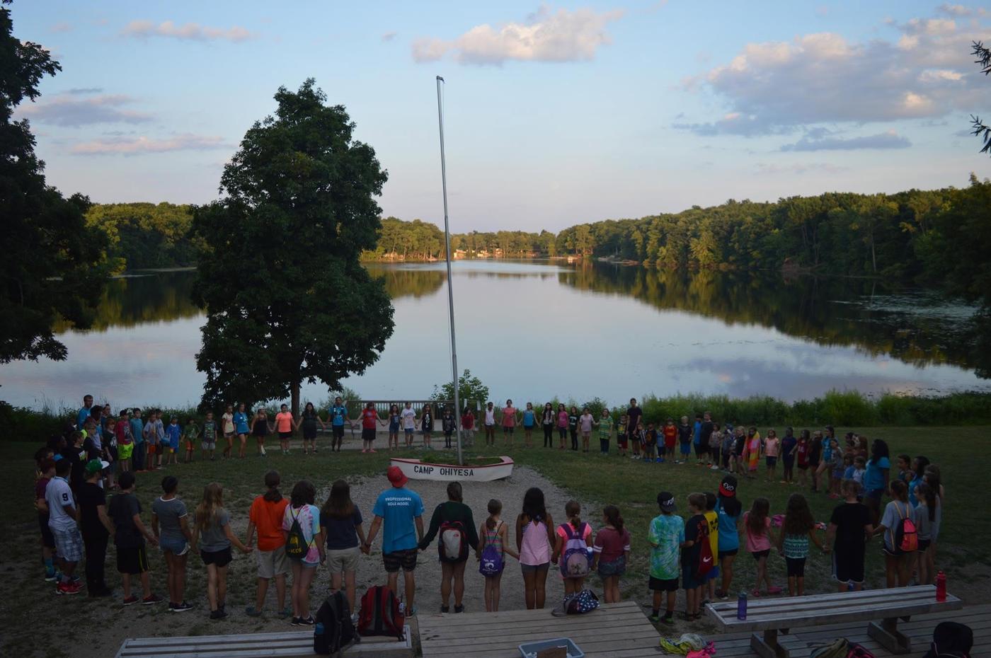 Campers and counselors holding hands in a giant circle on the shore of Fish Lake at Camp Ohiyesa at sunset