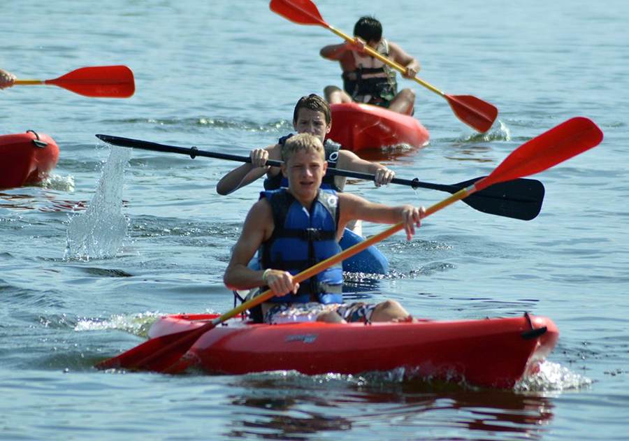 Campers paddling red kayaks on the lake
